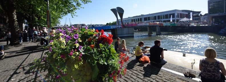 Harbourside in the sun. People sit on the embankment. The river reflects the light and in the background Pero